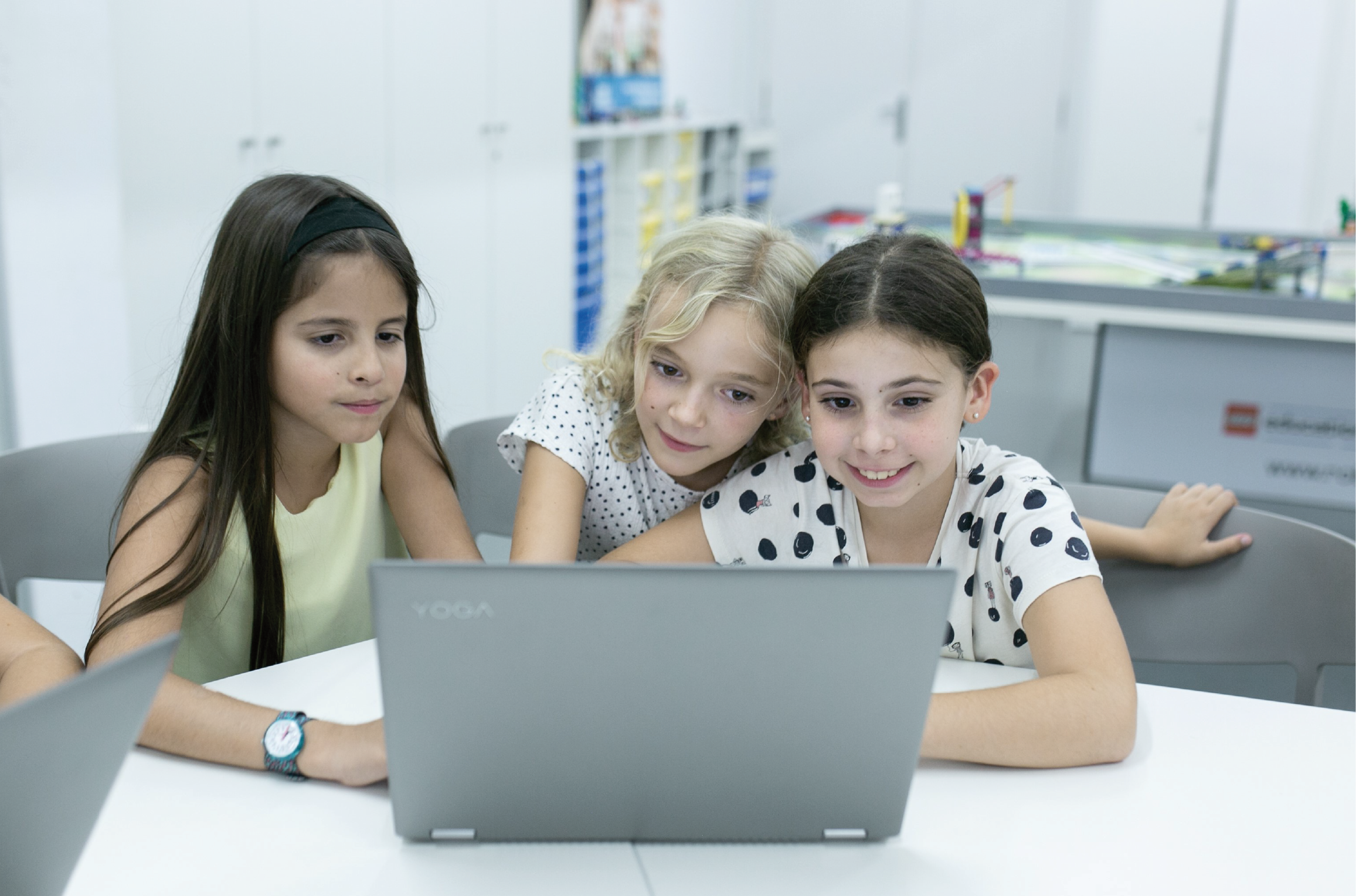 Tres niñas ante un portátil posiblemente en una webinar.